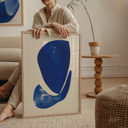 framed abstract art in blue held by a woman in a modern living room setting