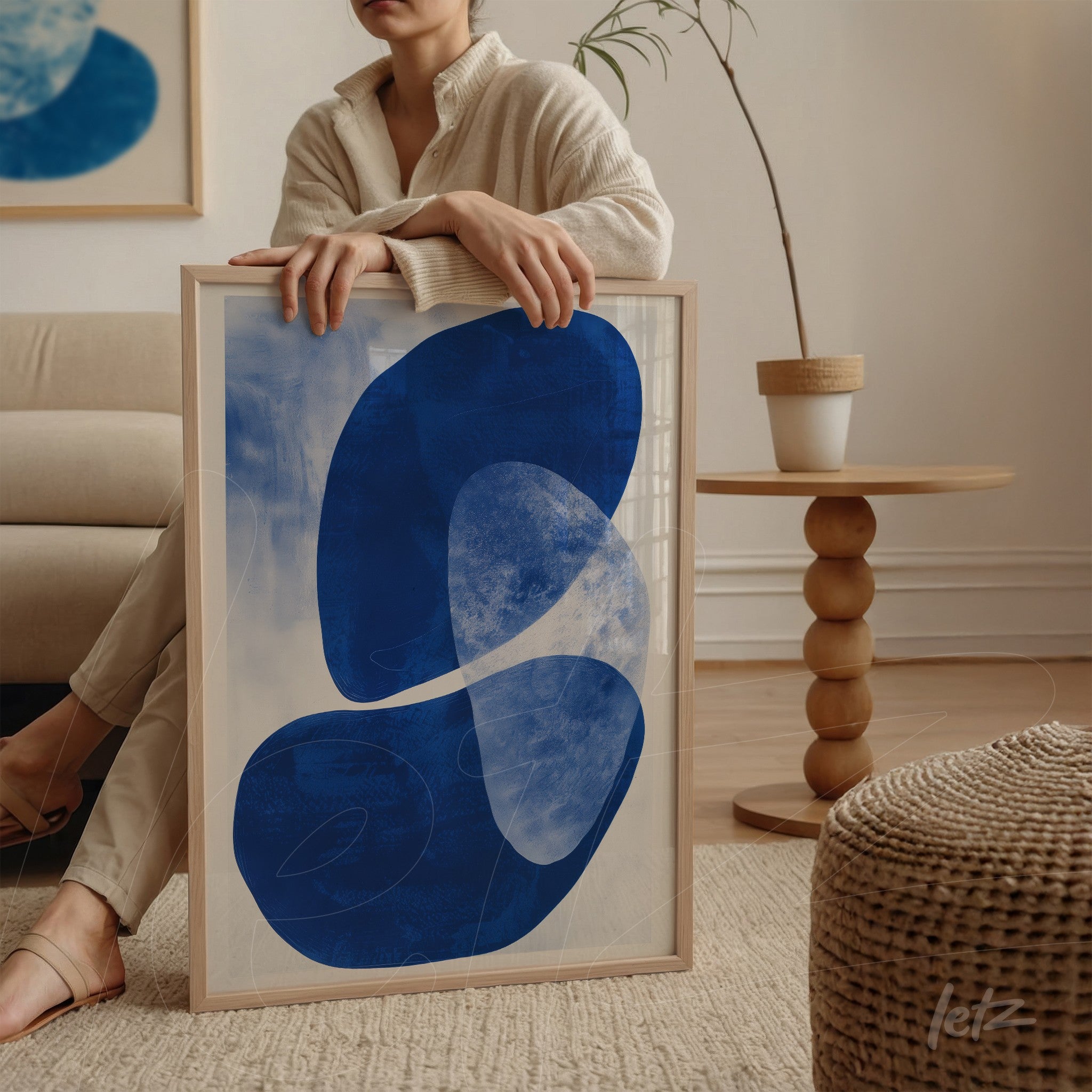 framed wall art featuring abstract blue shapes on a light background, leaning against a round table