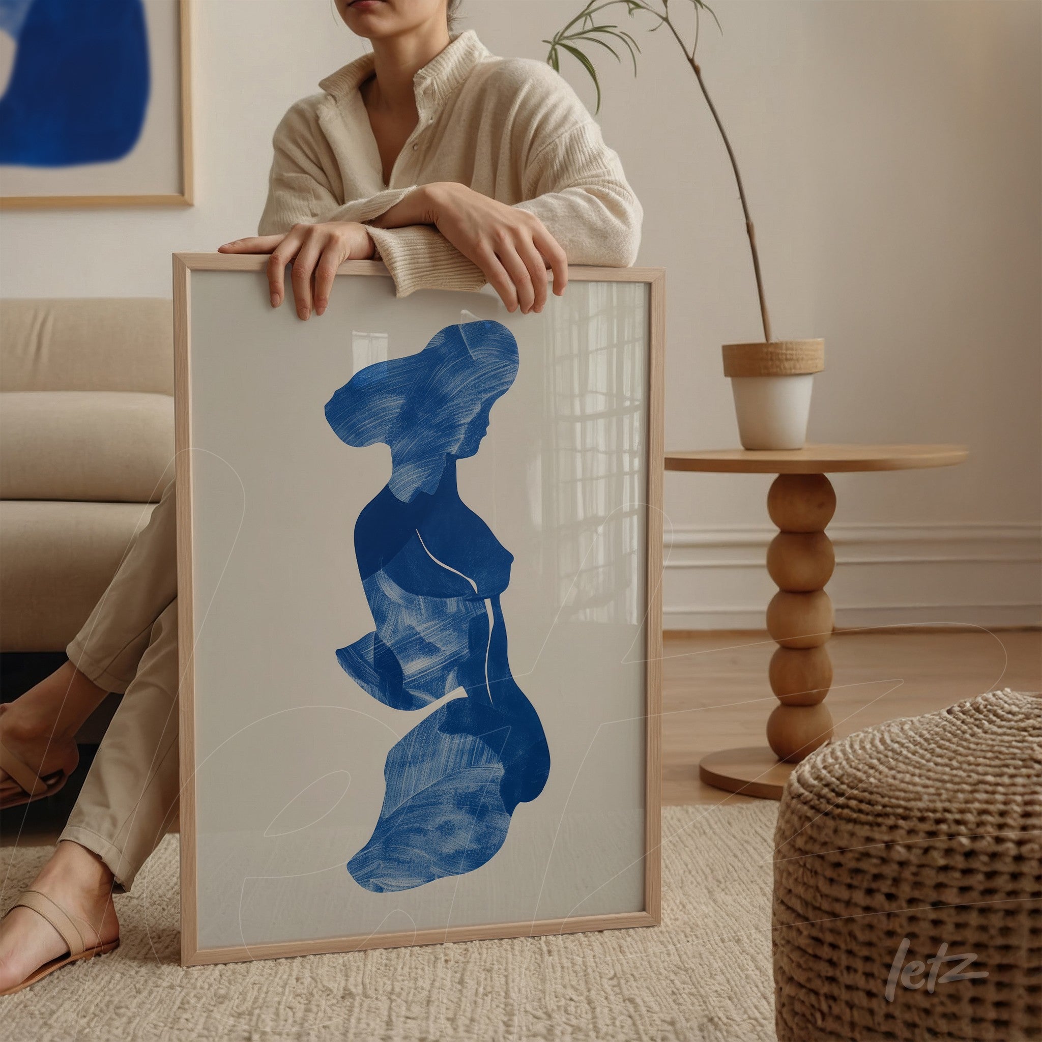 framed art of female silhouette in blue with light wood frame, leaning on a round table surface
