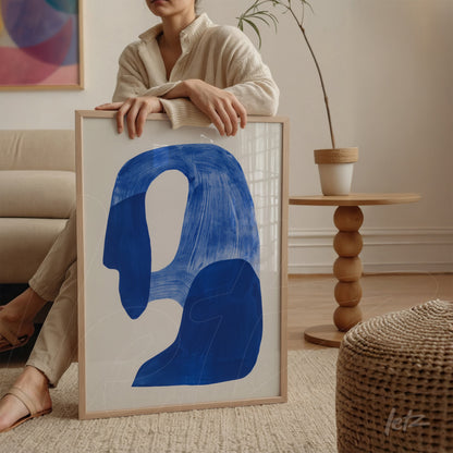 framed wall art featuring an abstract blue shape on a light background with a light wood frame in a minimalistic setting