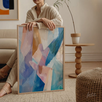 abstract wall art in shades of blue and pink with light wooden frame displayed on a wooden table