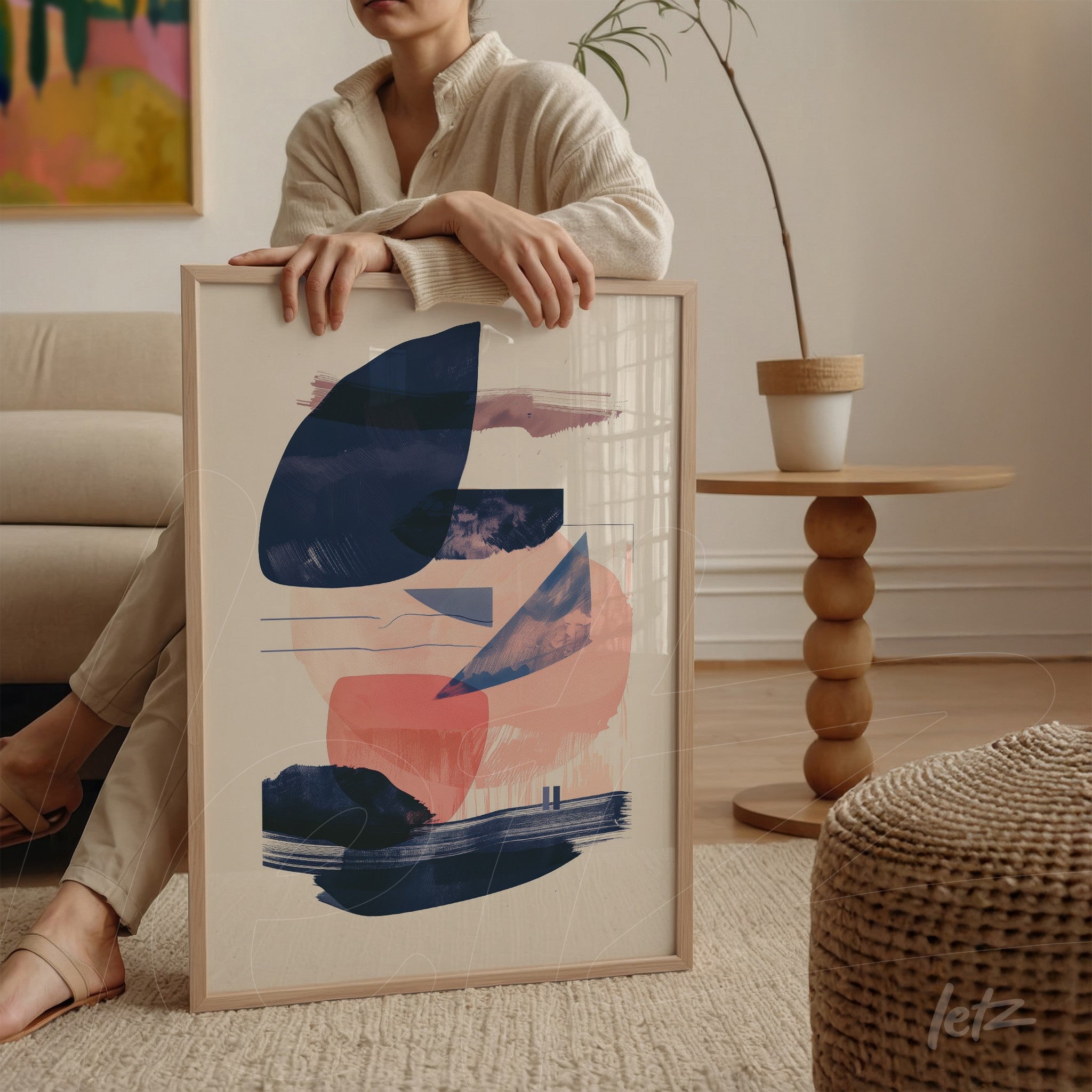 framed wall art featuring abstract design in navy blue and light pink, displayed on a table beside a plant