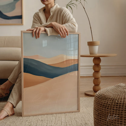 framed abstract art in neutral tones and blue, held by a woman in a well-lit room