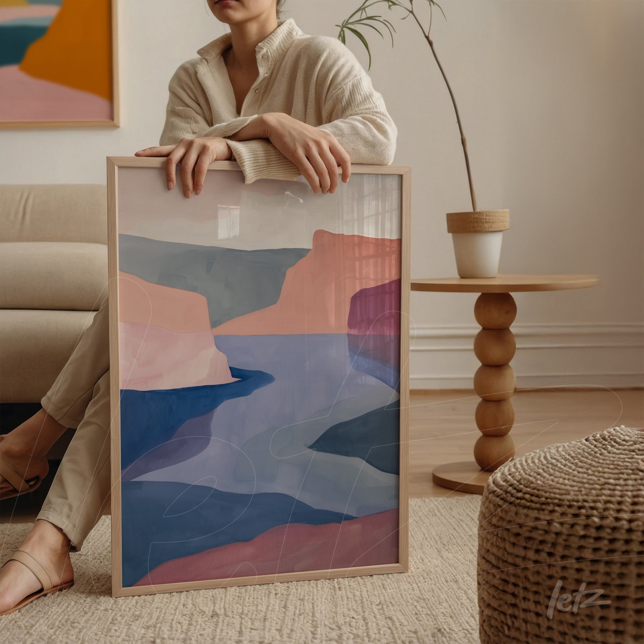 framed abstract wall art in shades of pink and blue displayed next to a person on a round table