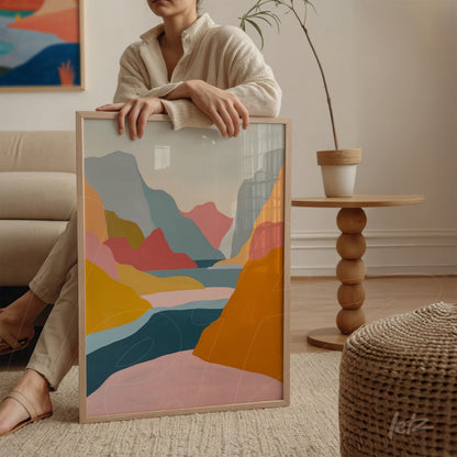 framed abstract art in shades of blue, pink, and orange held next to a woman beside a table