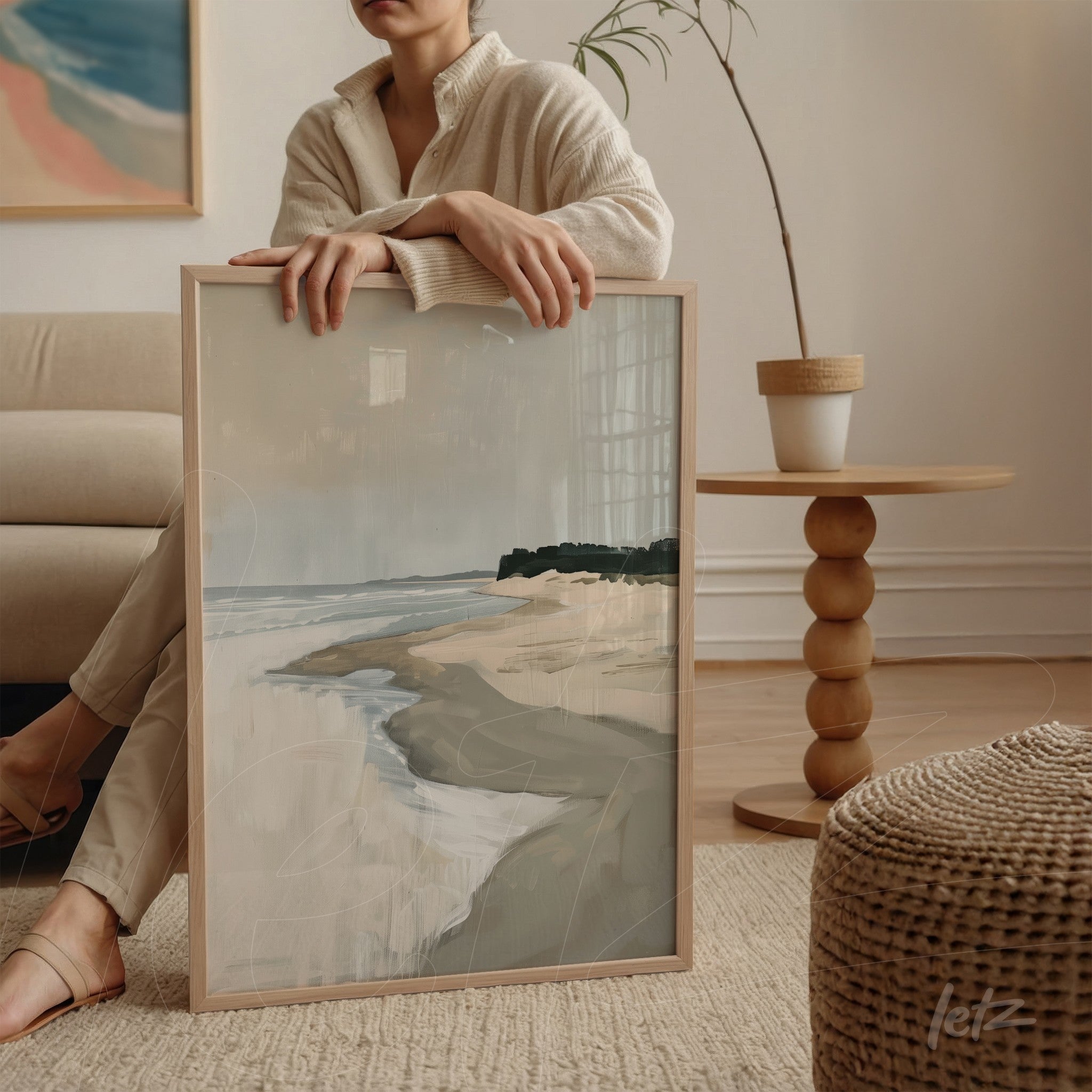 framed abstract art piece of a coastal landscape with light frame held by a person sitting on a sofa