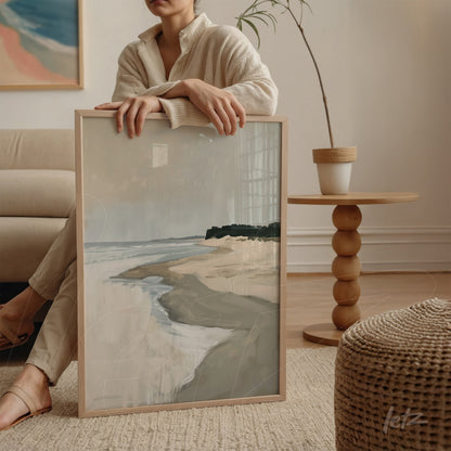 framed abstract art piece of a coastal landscape with light frame held by a person sitting on a sofa
