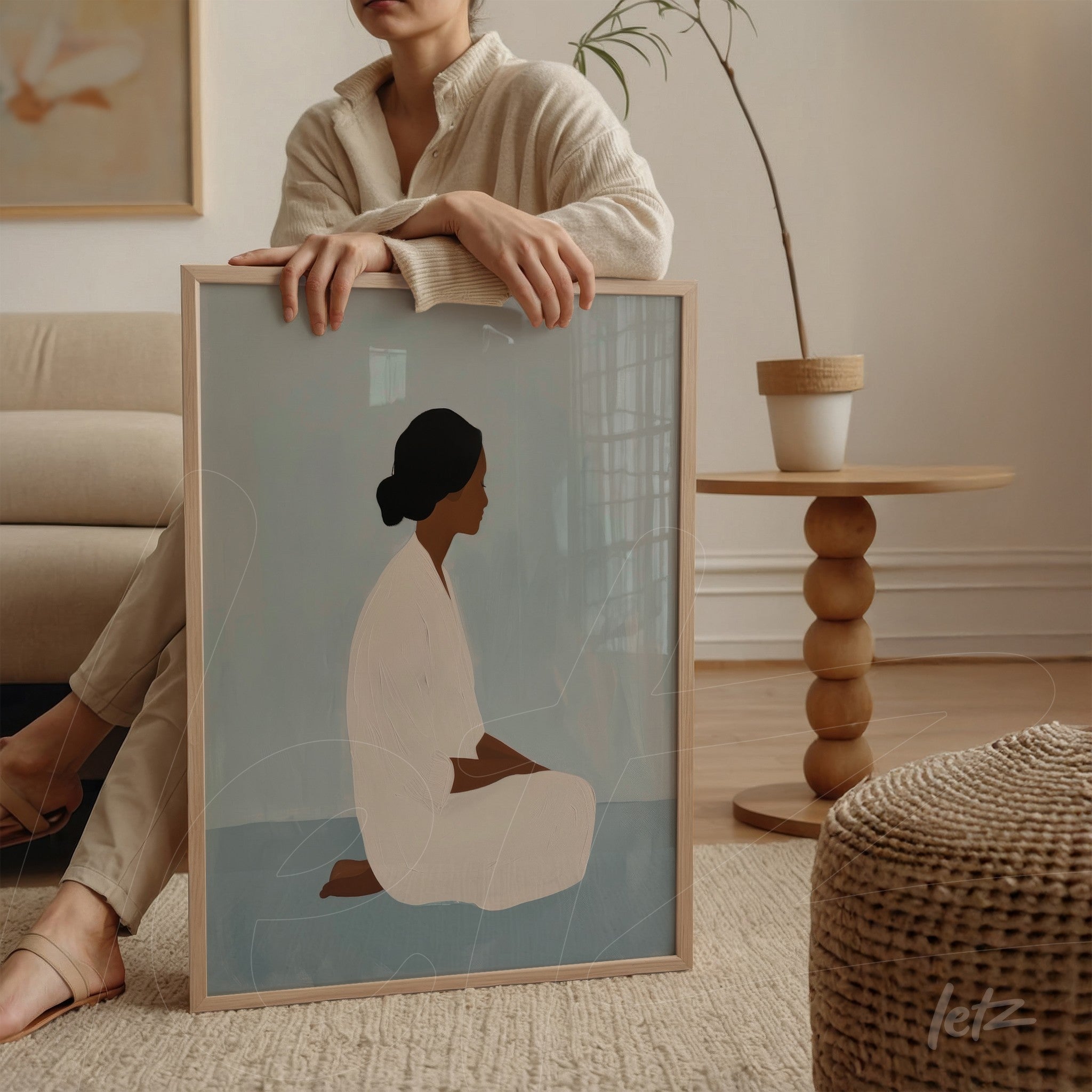 minimalist artwork of sitting female figure on blue background, framed in light wood, displayed next to a woman on a side table