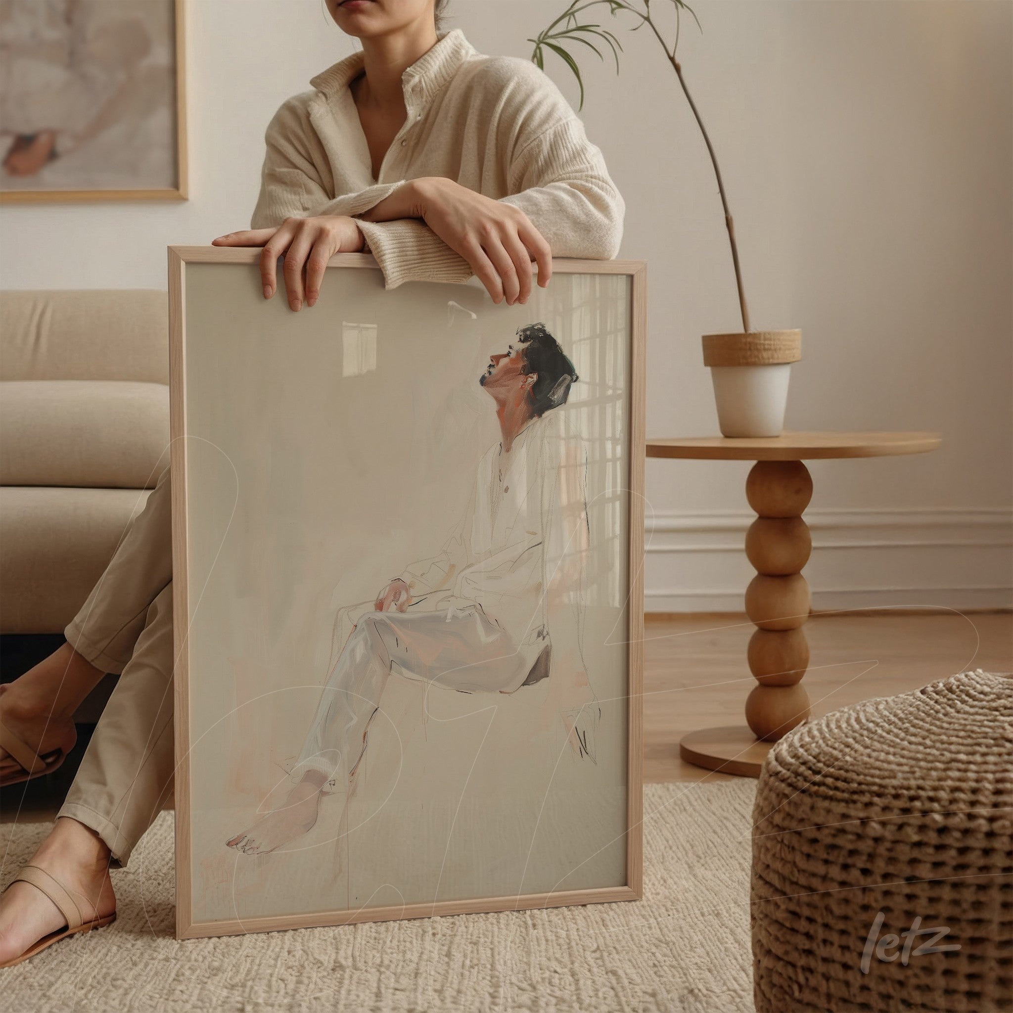 framed minimalist artwork of a human figure in light frame held against a woman's leg on a sofa
