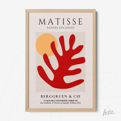 framed modern art piece featuring abstract cut-out shapes in red and orange against a beige background with a light wood frame