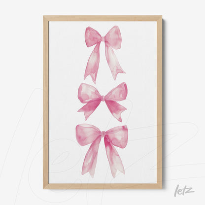 framed art featuring three pink watercolor bows displayed in a light wood frame